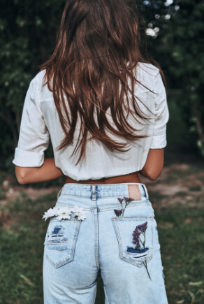 femme de dos portant des jeans avec fleurs dans les poches